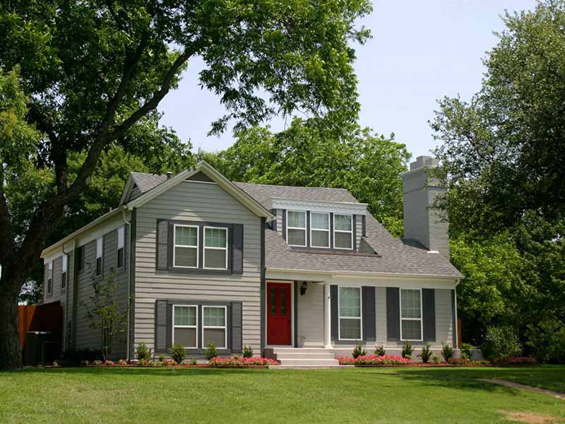 Front view of a gray home surrounded by many trees