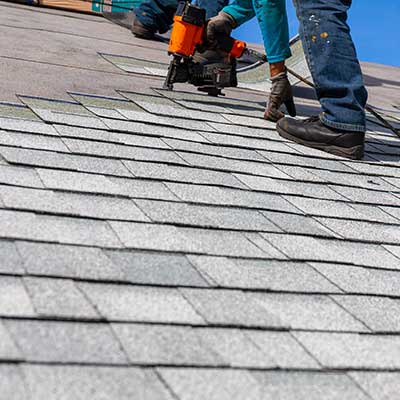Close up of worker installing new gray shingles on a residential roof with a nail gun